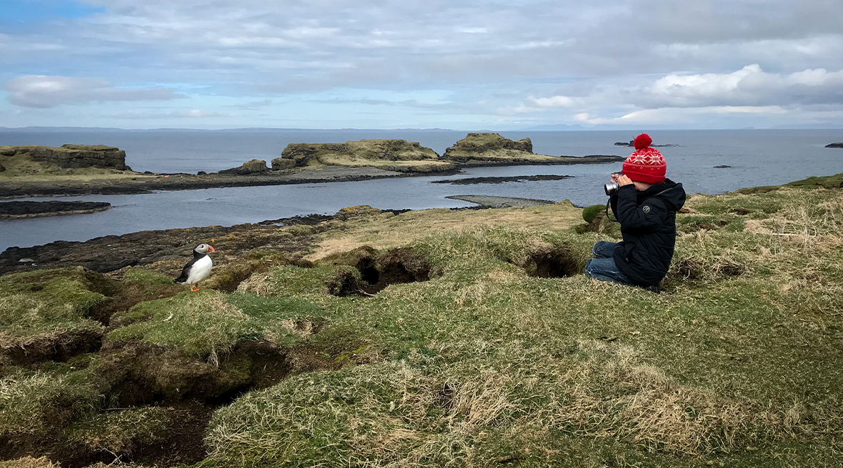Vader en zoon zitten in het gras naar een puffin te kijken: een vogel die veel voorkomt langs deze ruige kustlijn